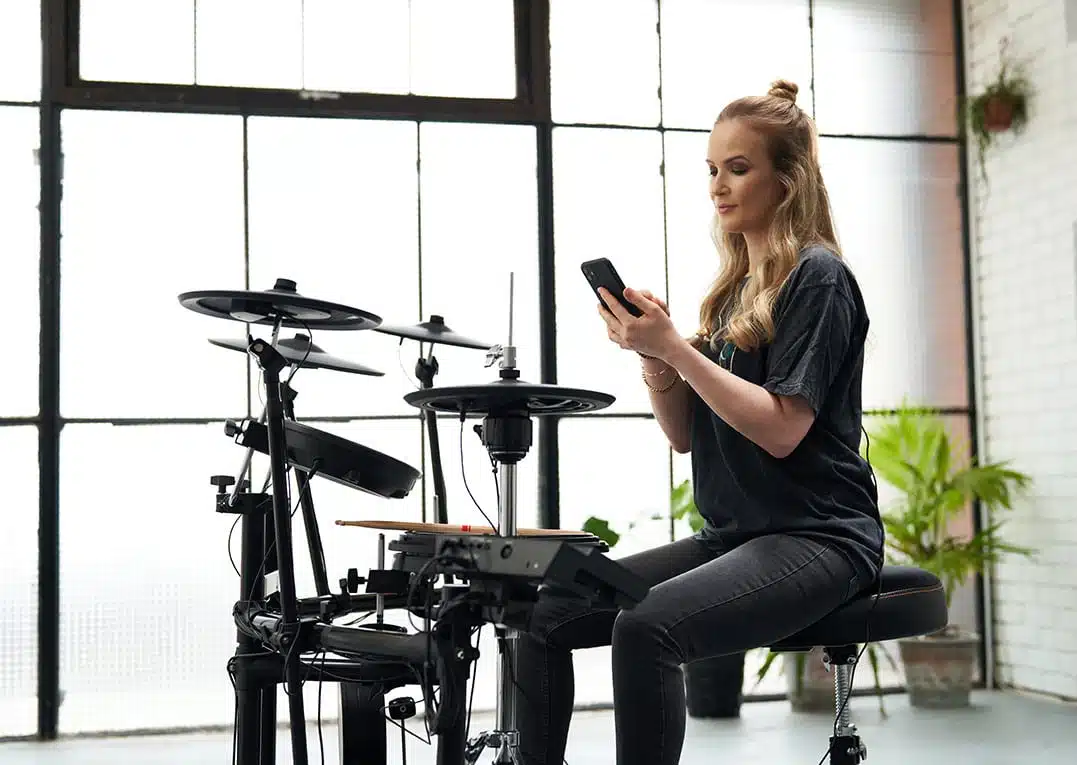 a woman sitting on a stool using a phone Roland TD-17KVX2 leguidedesbatteurs.com