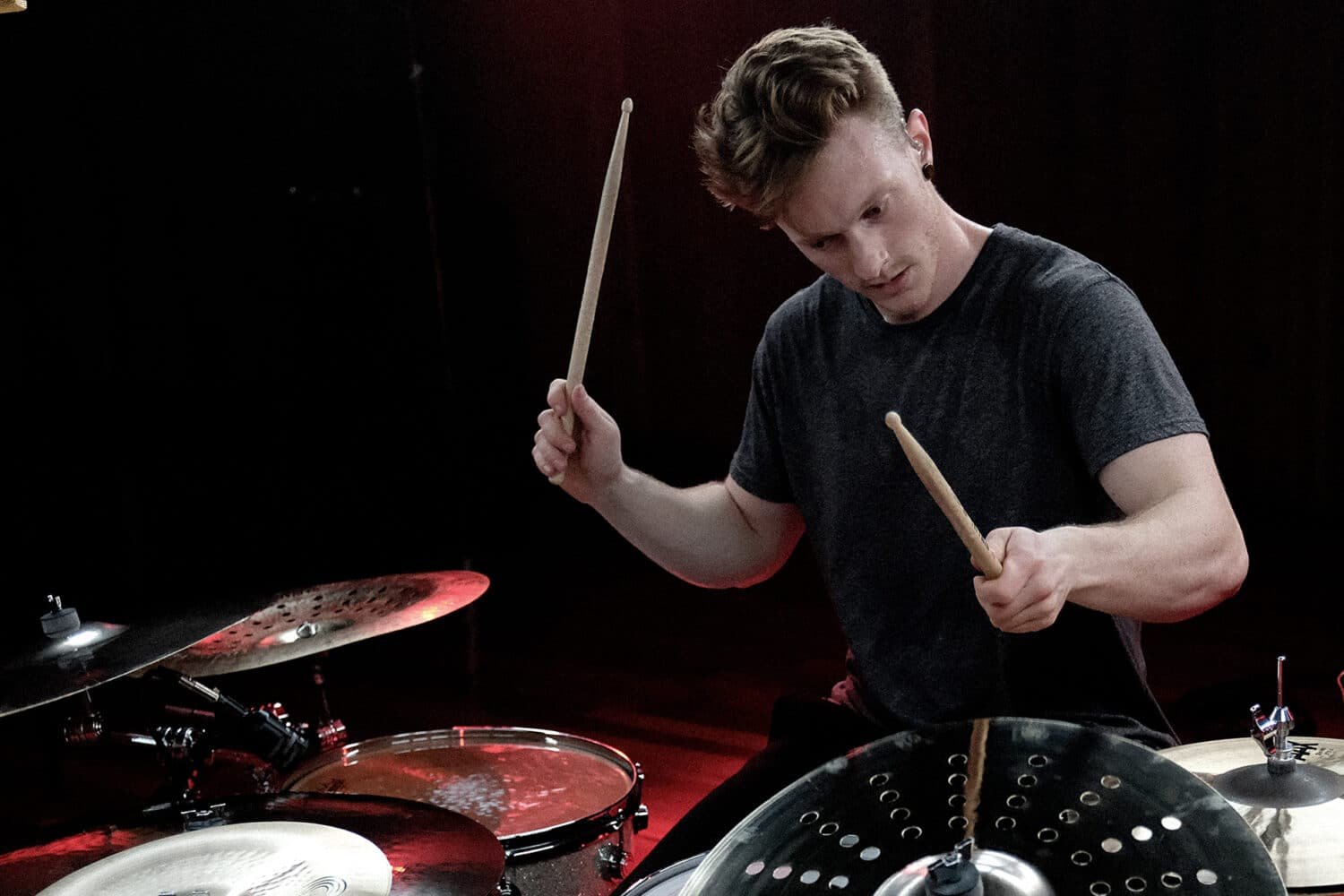 Batteur en plein jeu derrière ses cymbales Sabian AAX, sous un éclairage rouge en studio