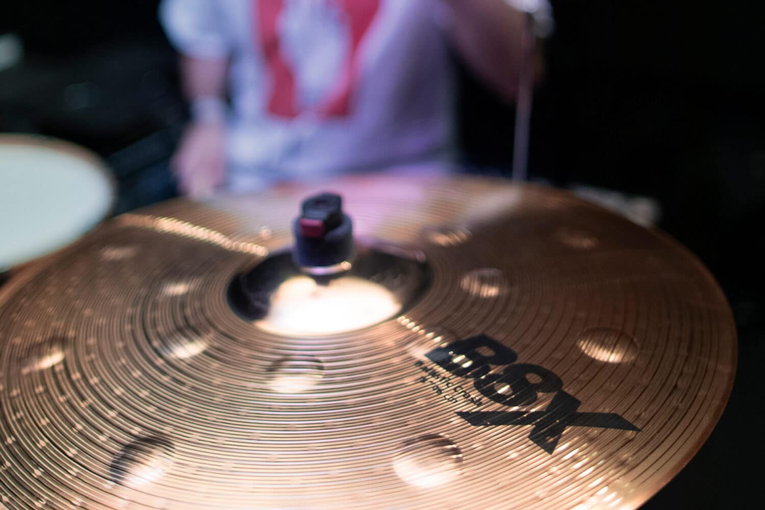 Gros plan sur une crash Sabian B8X, le batteur flou en arrière-plan