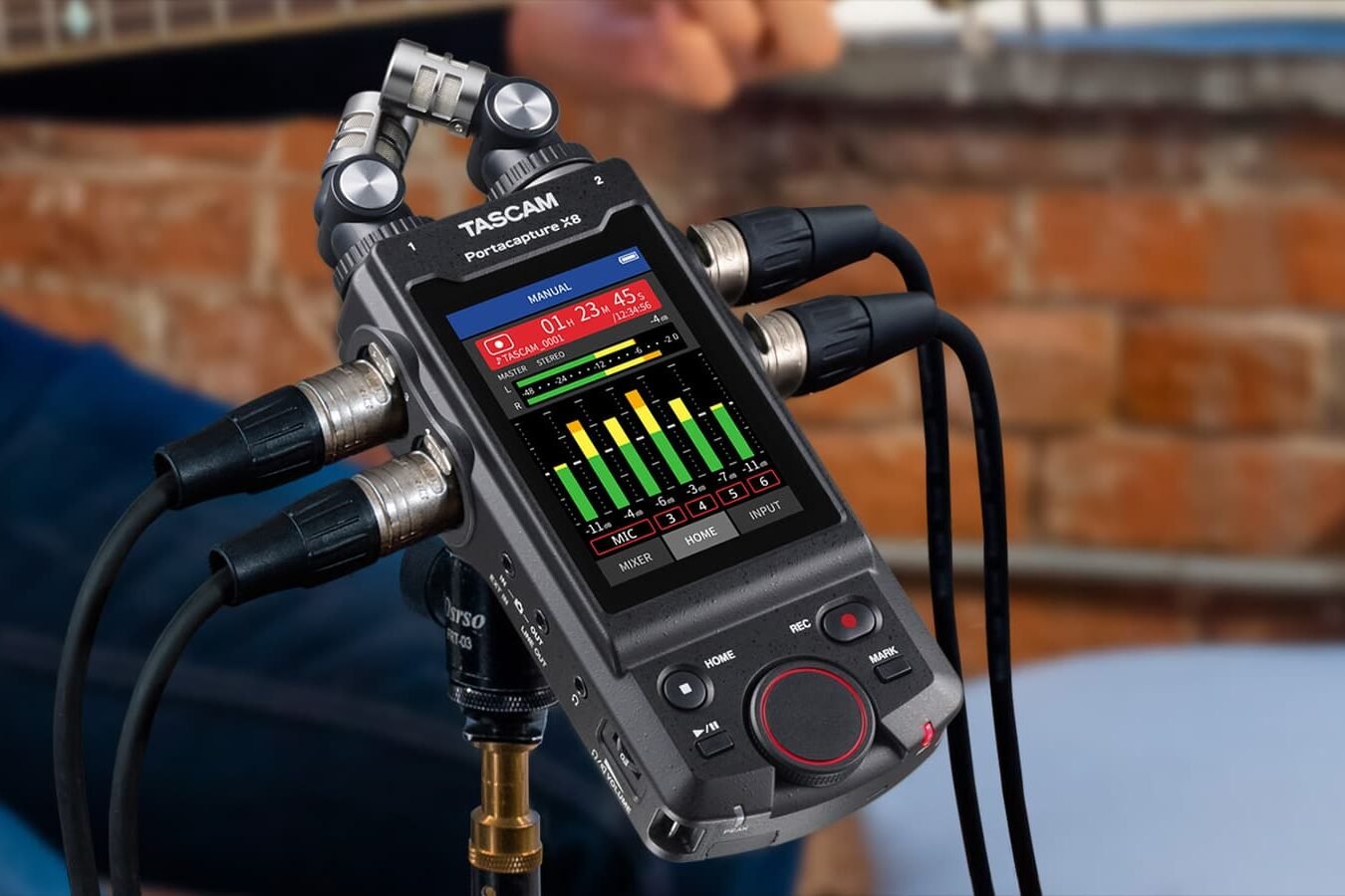 Tascam Portacapture X8 sur pied, câbles XLR branchés, devant un musicien jouant de la guitare