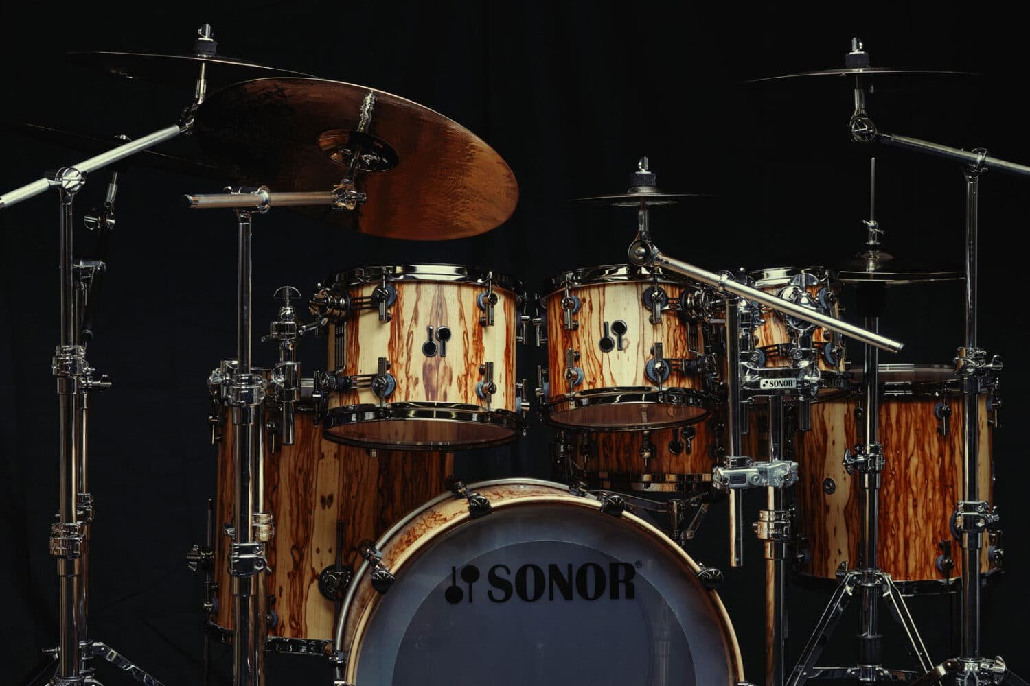 Batterie Sonor SQ2 en bois naturel installée sur une scène sombre avec cymbales et pieds